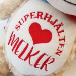 Nærbilde av brodert navn på magen til superhelt-teddybjørnen